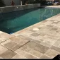 the outdoor area of a house where there is a pool and the deck around the pool is floored with travertine pavers